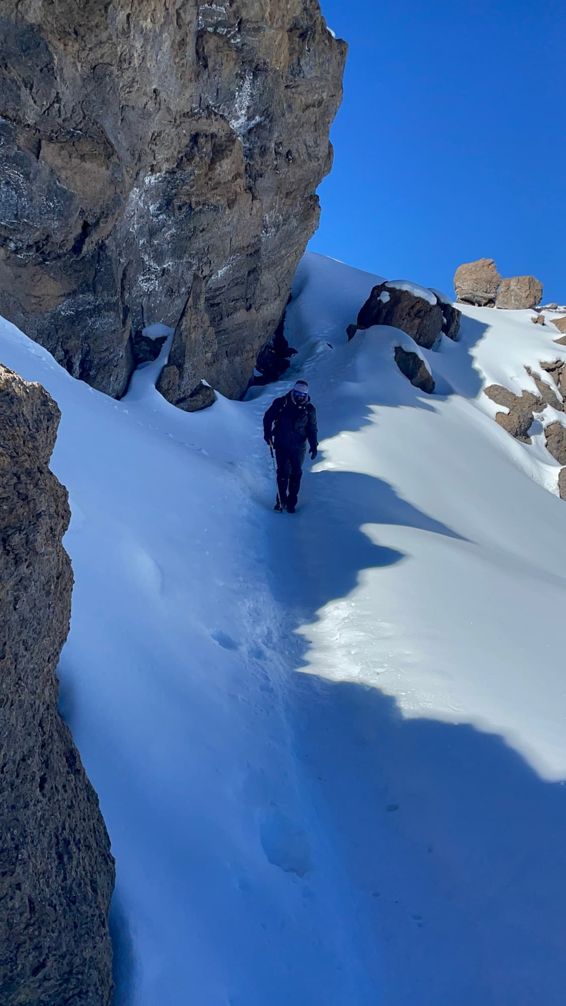 A climber descending a snow-filled gully between dark lava cliffs