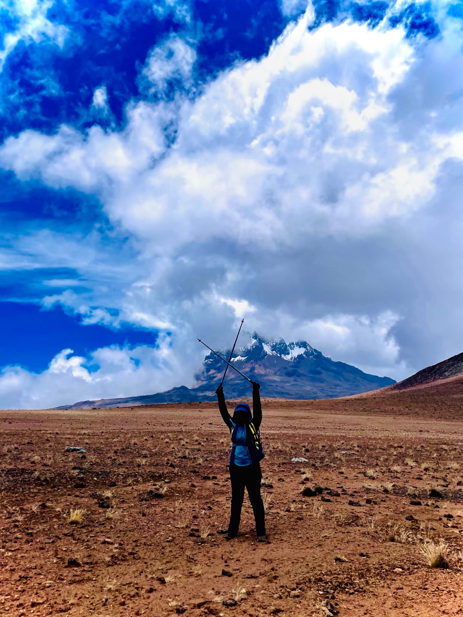 A hiker raising trekking poles in celebration in the alpine desert below Mawenzi