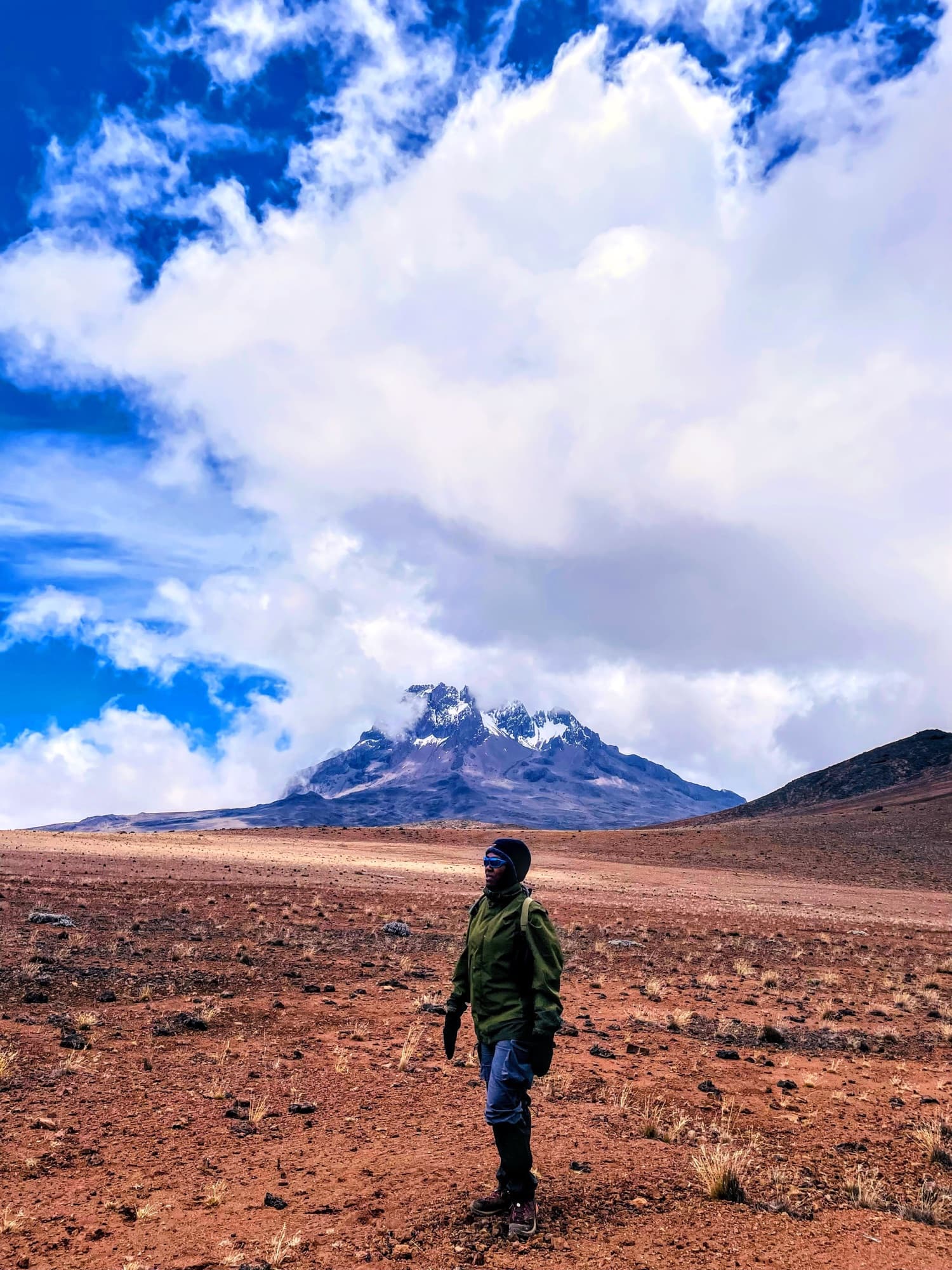 A guide standing in the red-brown alpine desert with Mawenzi behind