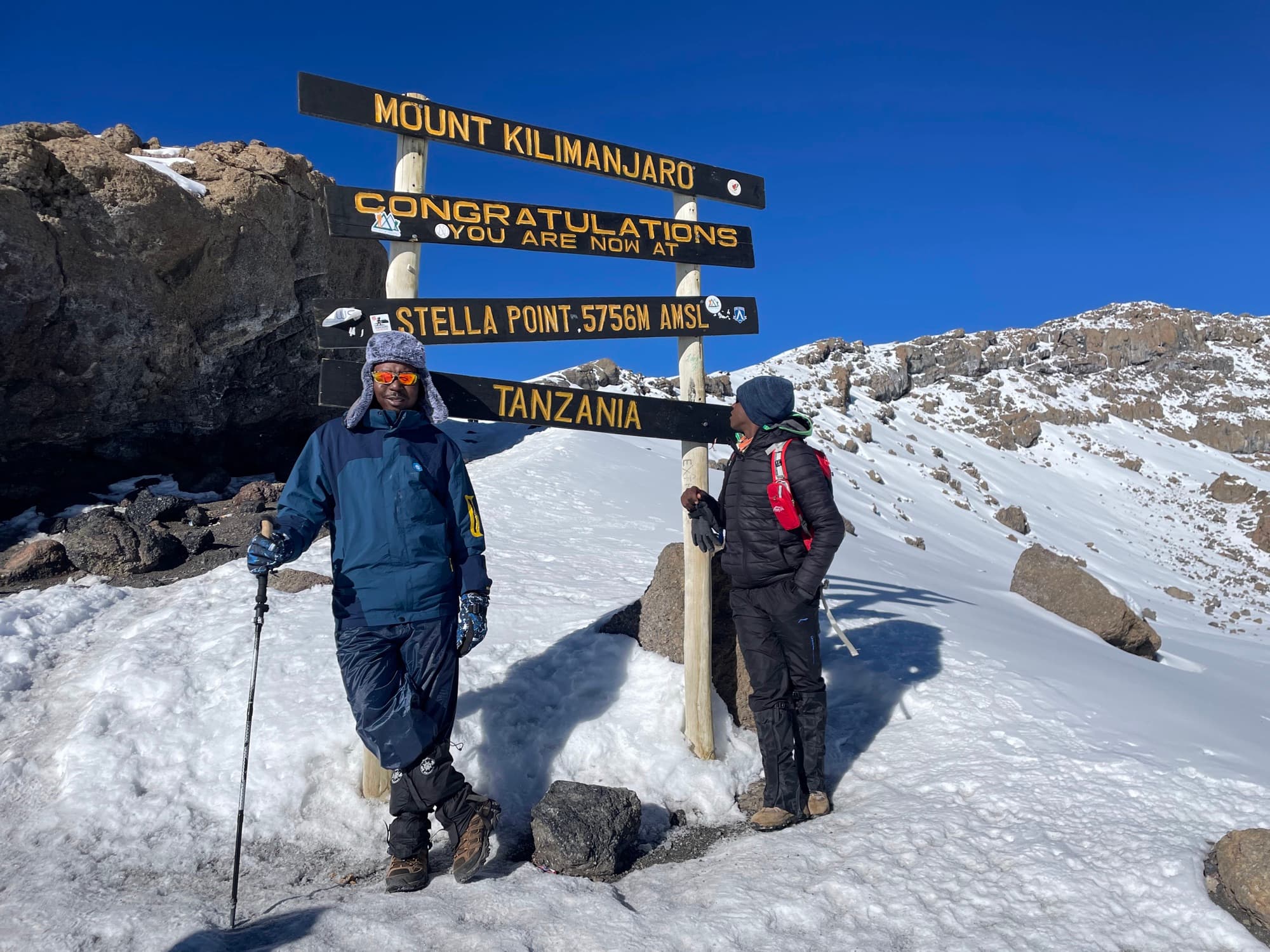 Two trekkers talking beside the Stella Point sign above the snowfields