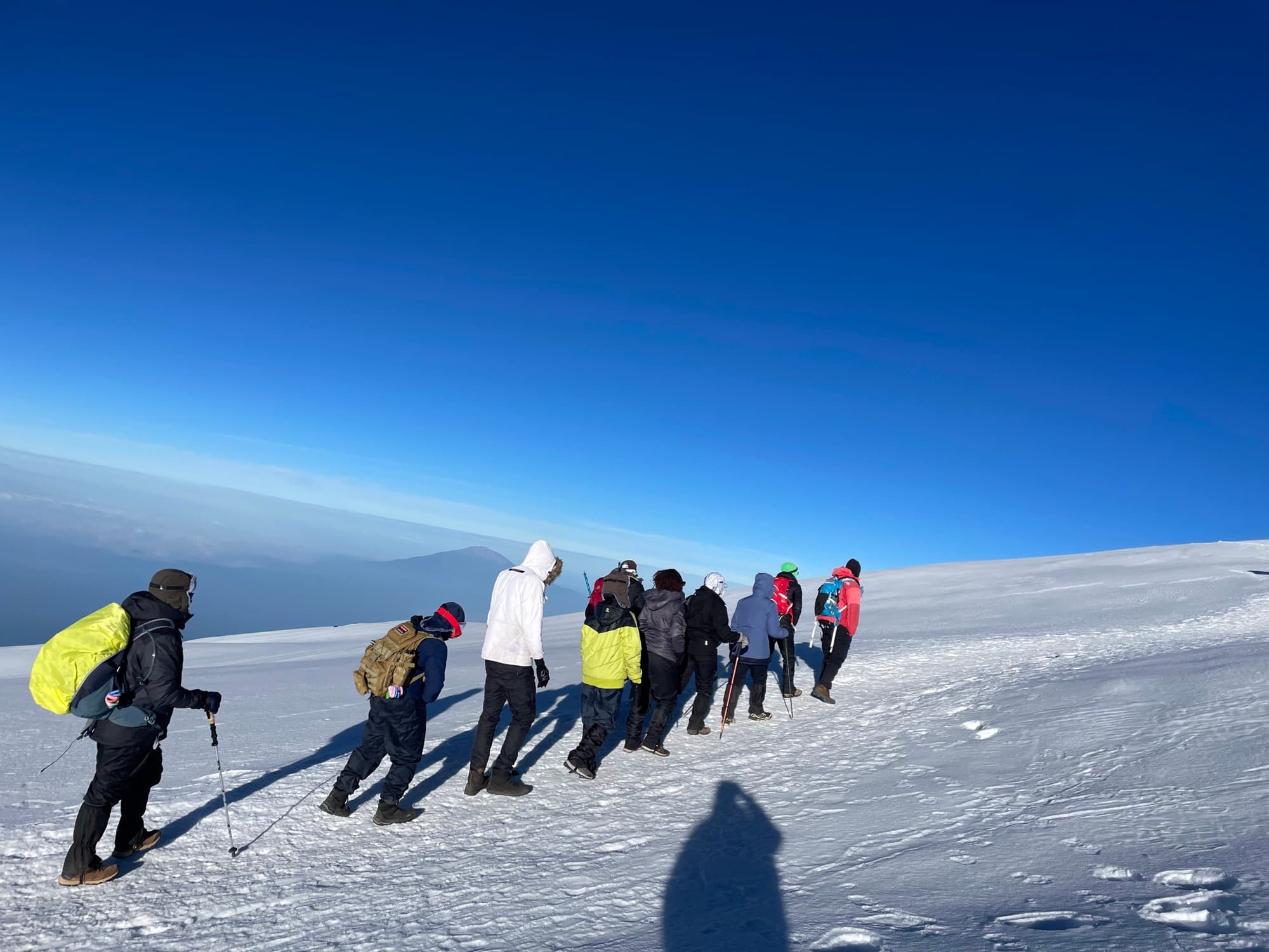 Long dawn shadows of trekkers walking the summit snow ridge