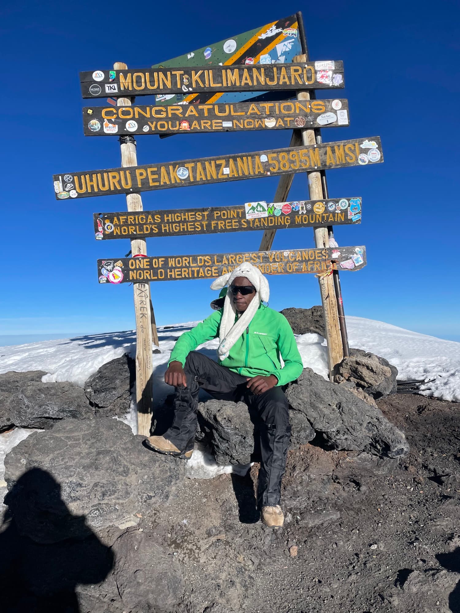 A trekker seated on the summit rocks beneath the Uhuru Peak sign