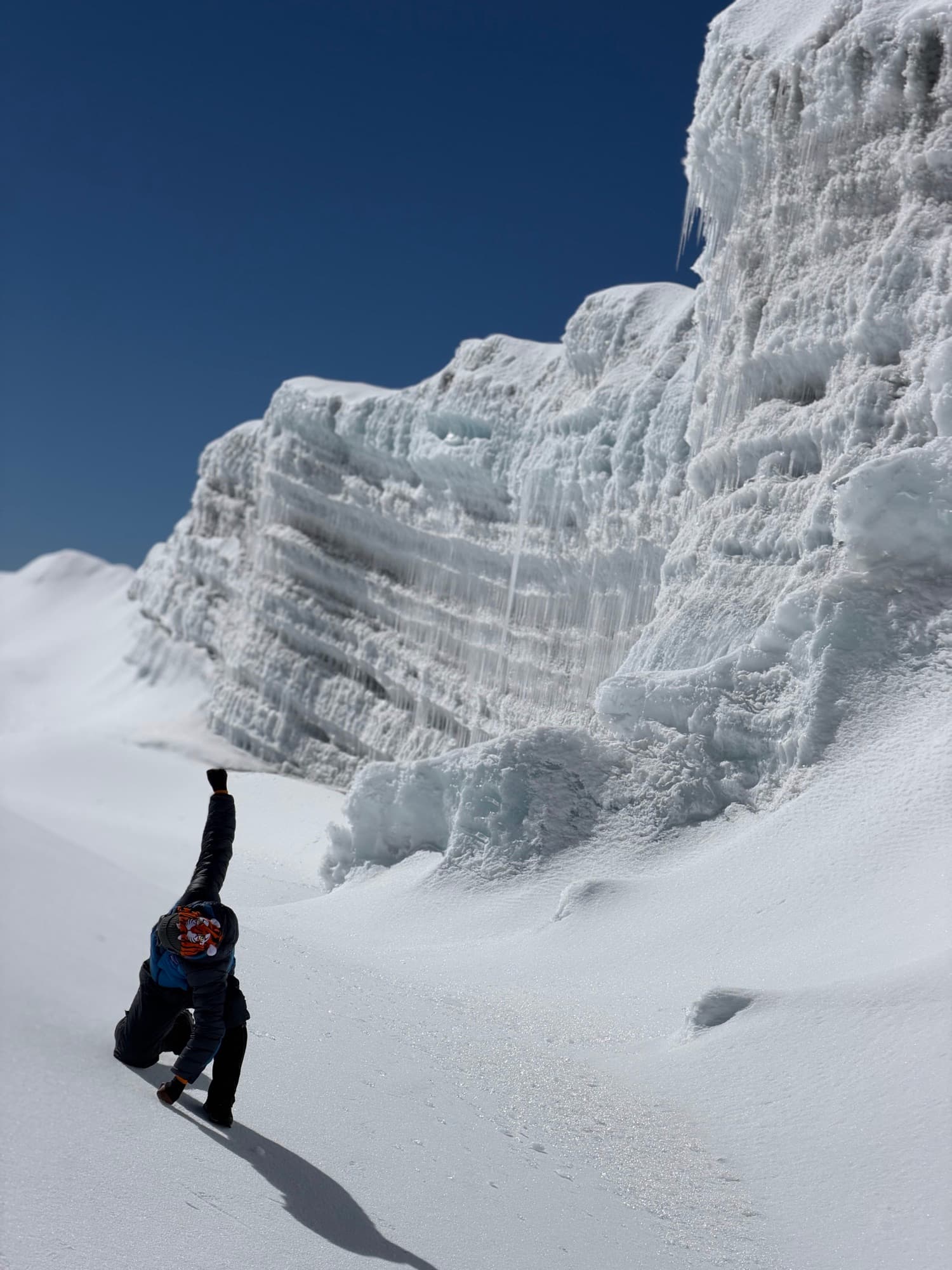 A climber saluting beneath the towering ice walls of Kilimanjaro's summit glaciers