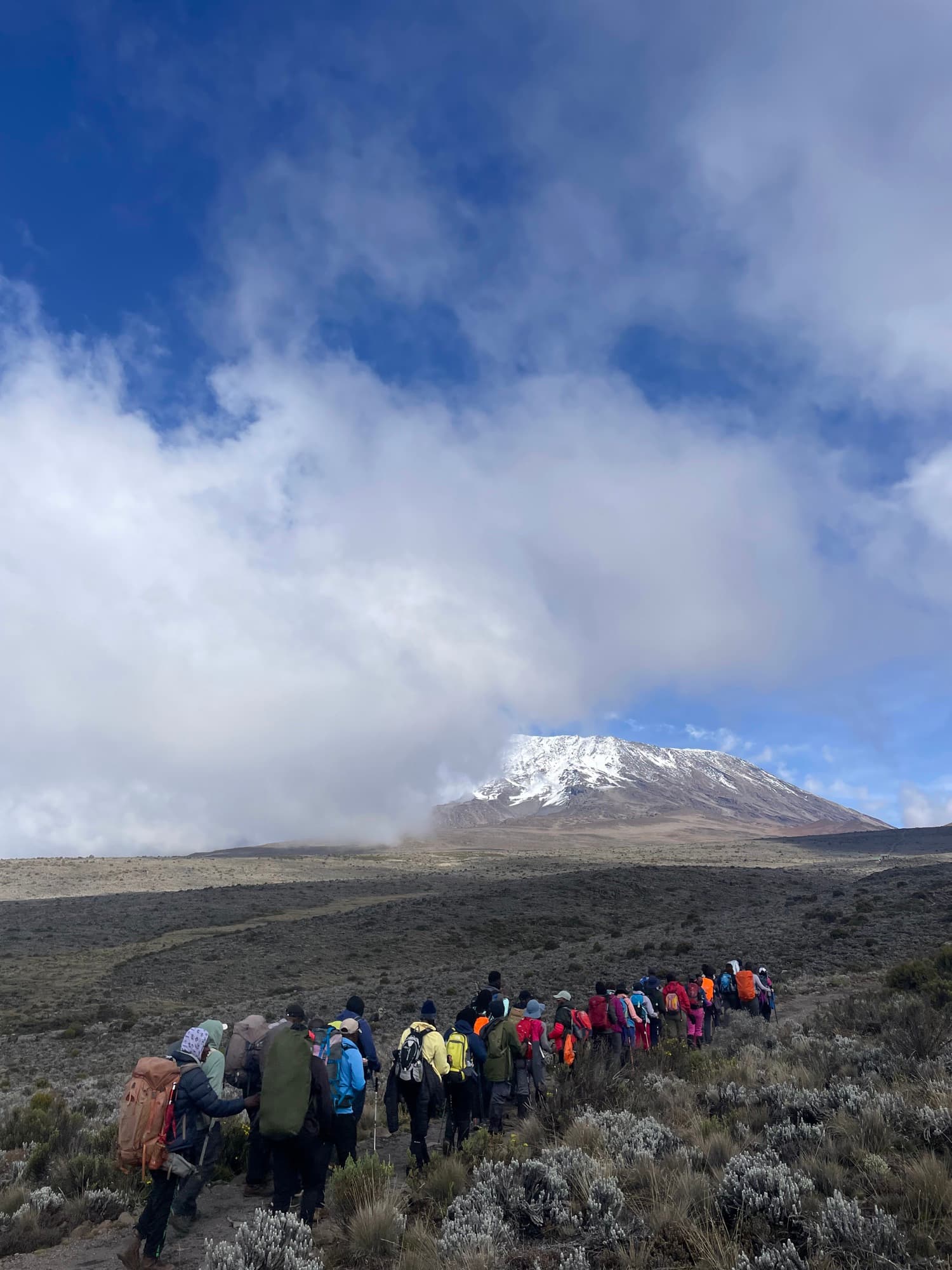 A long line of trekkers heading toward Kibo as clouds clear off the summit