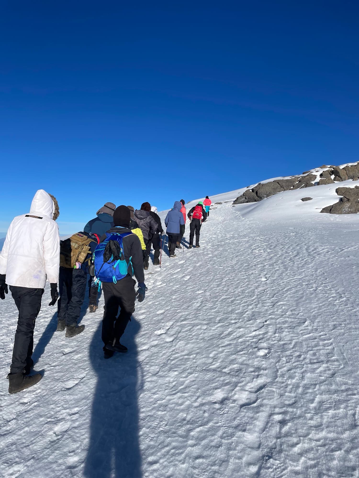 Trekkers climbing a snow slope near the crater rim under a deep blue sky